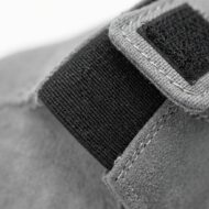 Close-up of a gray fabric strap with a black Velcro fastener on a gray suede surface, showing stitching details.