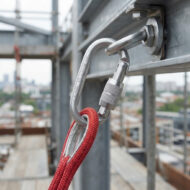 Silver metal carabiner attached to a red safety rope secured to scaffolding at a construction site.