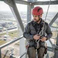 Construction worker in a red helmet and safety harness on a steel framework high above ground.