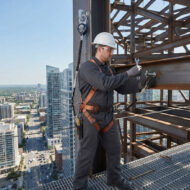 Construction worker in a hard hat and safety harness tightening a bolt on a steel beam high above a city skyline.