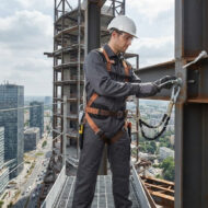 Construction worker in a hard hat and safety harness secures a steel beam at a high-rise construction site.