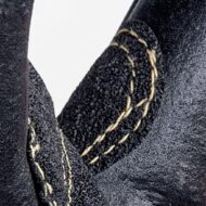 Close-up of a black leather boot, showing beige stitching along a seam.