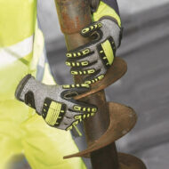 Worker in a high-visibility jacket grips a rusted auger bit with gloved hands for digging.