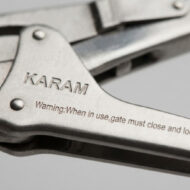 Close-up of a metal tool with engraved 'KARAM' and warning text along the lever edge (industrial hardware).