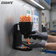 Worker in gray gloves loading orange capsules from a bottle into a wall-mounted dispenser.