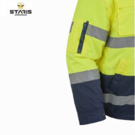 Close-up of a neon yellow and navy high-visibility work jacket with reflective bands and a zip pocket on the sleeve; Staris Workwear logo in the top-left corner.