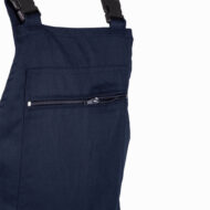 Close-up of navy blue overalls showing a horizontal zippered pocket and adjustable shoulder straps.
