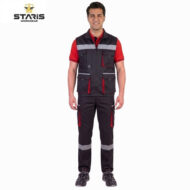 Man wearing a black utility vest with red trim and multiple pockets, red polo underneath, reflective bands on chest and legs, standing neutral.