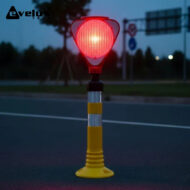 Red warning light atop a yellow portable stand on a road at dusk, signaling caution in a construction/roadwork area.