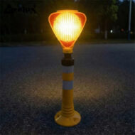 Orange warning beacon atop a striped yellow-and-white post on a dark road at dusk, signaling construction or restricted area.