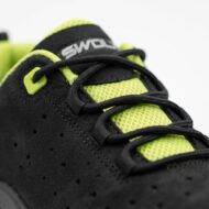 Close-up of a black athletic sneaker with neon lime tongue and black laces, showing a perforated side panel.